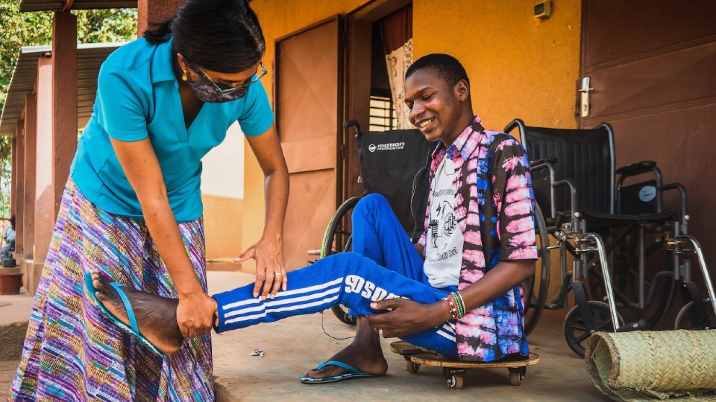 Suja Brane fitting a leg brace for a young man in a wheelchair