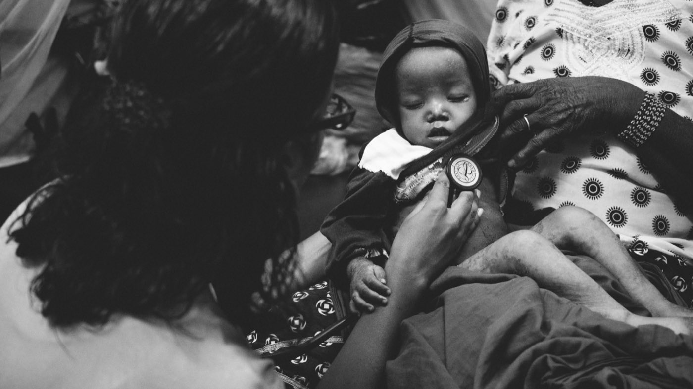 Suja Brane listening to a young child's chest with a stethoscope
