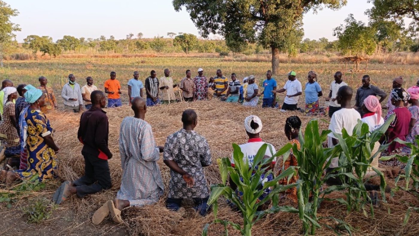 Farmers kneeling in a circle to pray at the edge of a field