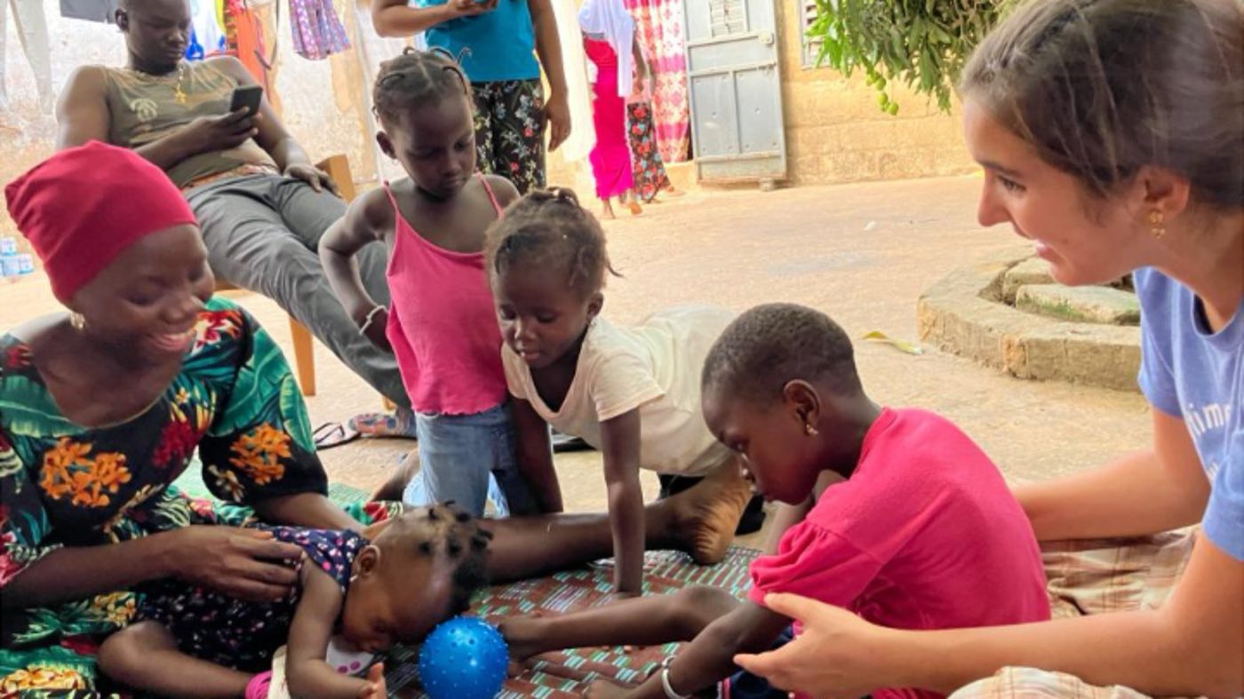 Children and a visitor playing with a ball beside a child lying on a mat