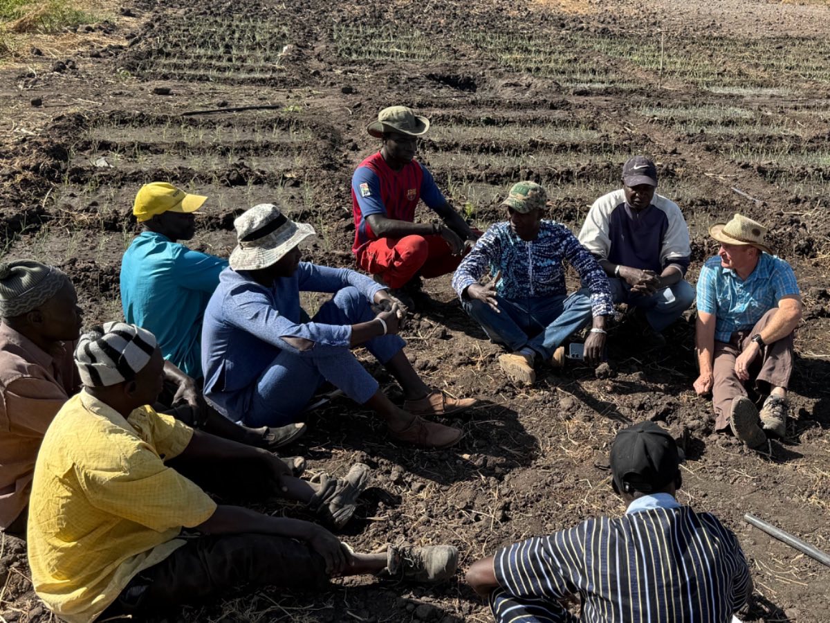 Tom Brane sitting in a field talking with a circle of farmers