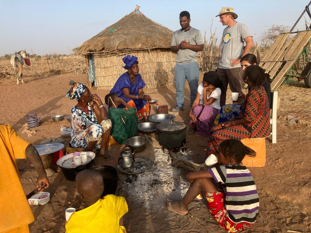 Tom and Suja Brane sitting with a village family around a cooking fire