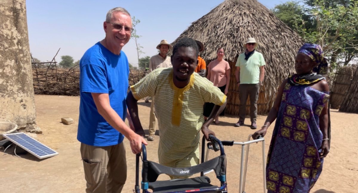 A young man walking with a new walker, supported by visitors and his mother