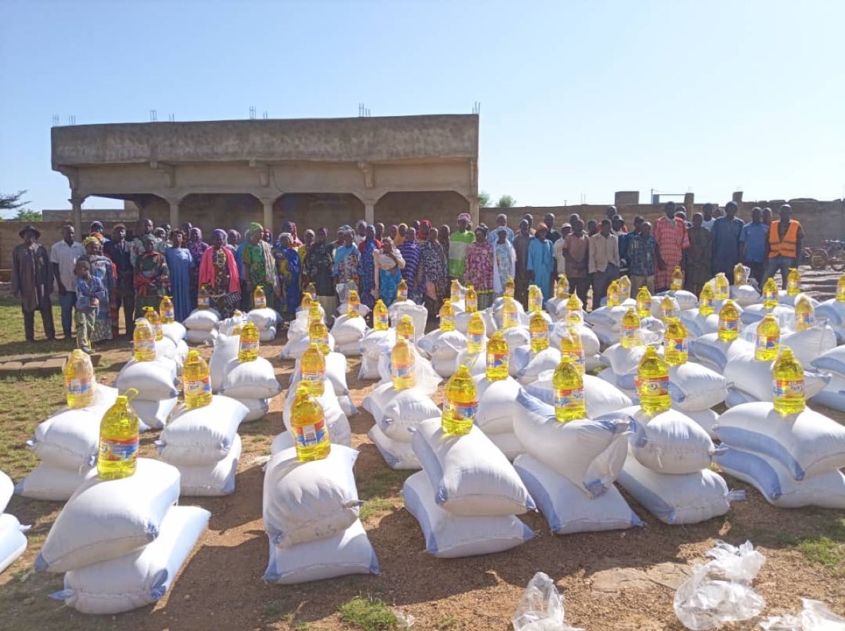 Villagers standing behind sacks of grain and bottles of oil ready for distribution