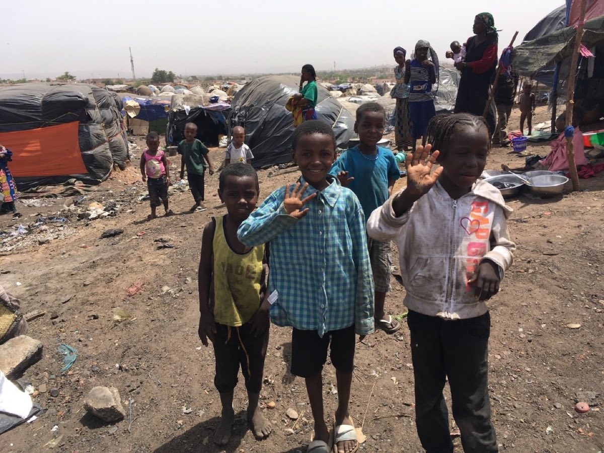 Children waving outside shelters in a displacement camp
