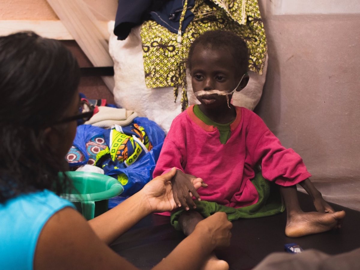 Suja Brane holding the hand of a child with a feeding tube
