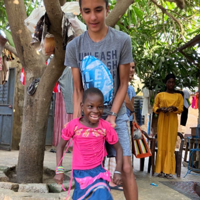 A teenager helping a girl walk in a village courtyard