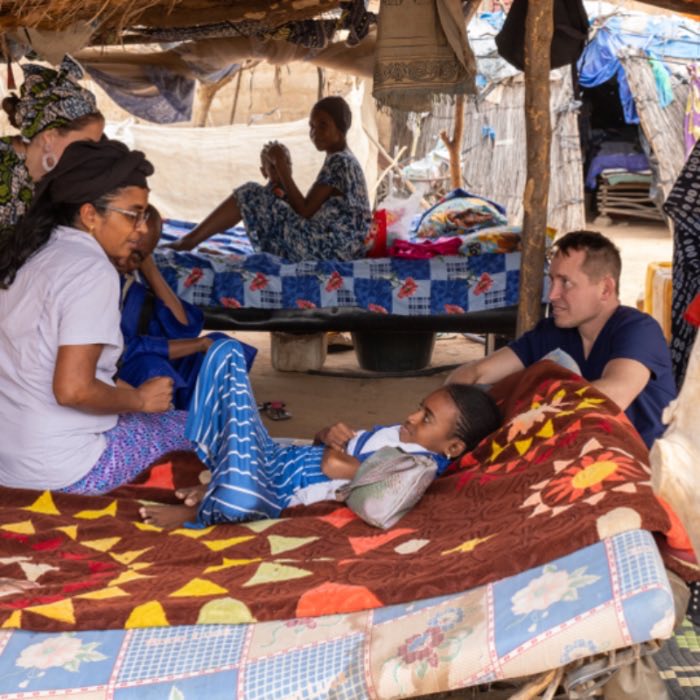 Tom and Suja Brane visiting a patient resting on a mat at home