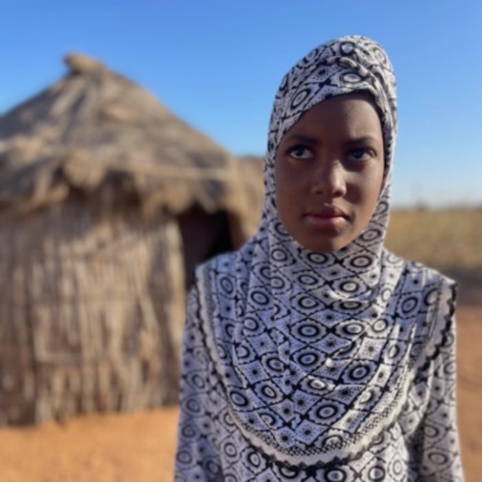 A young woman standing in front of a thatched hut