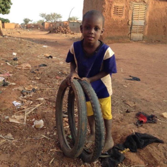 A boy holding two bicycle tires in a village street